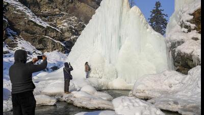 Tourists take pictures near icicles formed due to a water pipe leak at Tangmarg in Baramulla district, Jammu and Kashmir, on Wednesday. (PTI)
