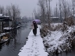 A Kashmiri walks on a snow-covered footbridge as boatmen row past her in the interiors of Dal Lake in Srinagar, Indian controlled Kashmir, Jan. 6, 2025. 