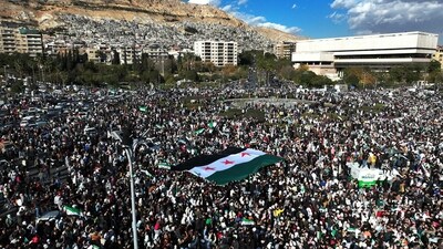 An aerial photo shows crowds of Syrians raising a giant independence-era flag, used by the opposition since the uprising began in 2011, as they celebrate the fall of Bashar al-Assad's iron-fisted rule earlier this week at the central Umayyad Square in Damascus on December 13, 2024. (AFP)