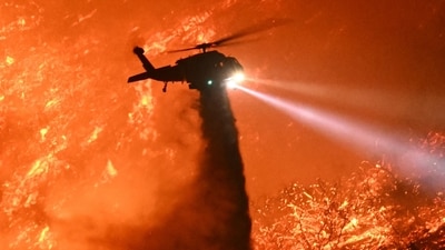 A fire fighting helicopter drops water as the Palisades fire grows near the Mandeville Canyon neighborhood and Encino, California, on January 11, 2025. The Palisades Fire, the largest of the Los Angeles fires, spread toward previously untouched neighborhoods January 11, forcing new evacuations and dimming hopes that the disaster was coming under control. Across the city, at least 16 people have died as multiple fires have ripped through residential areas since January 7, razing thousands of homes in destruction that US President Joe Biden likened to a "war scene." (Photo by Patrick T. Fallon / AFP) (AFP) A fire fighting helicopter drops water as the Palisades fire grows near the Mandeville Canyon neighborhood and Encino, California, on January 11, 2025. The Palisades Fire, the largest of the Los Angeles fires, spread toward previously untouched neighborhoods January 11, forcing new evacuations and dimming hopes that the disaster was coming under control. Across the city, at least 16 people have died as multiple fires have ripped through residential areas since January 7, razing thousands of homes in destruction that US President Joe Biden likened to a "war scene." (Photo by Patrick T. Fallon / AFP) (AFP)