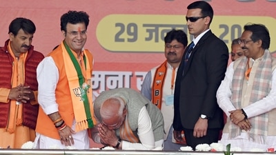 Prime Minister Narendra Modi touches the feet of BJP Patparganj assembly seat candidate Ravindra Singh Negi during a public meeting for the Delhi assembly elections at Yamuna Khadar, Ghonda, in New Delhi on Wednesday. (Sanjeev Verma/ Hindustan Times)