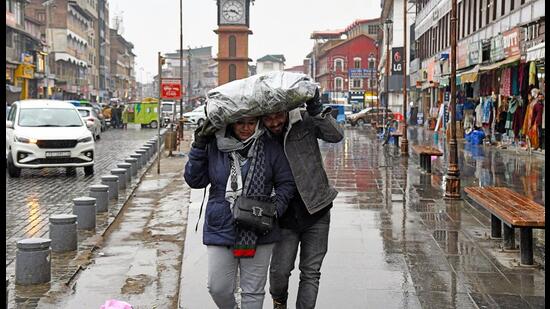 People walk amid rain in Srinagar on Friday. (ANI)