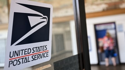 The United States Postal Service (USPS) logo is displayed on a door as a postal customer uses a self-service mail shipping kiosk to ship a package at a USPS post office on August 28, 2024 in Redondo Beach, California. (AFP)