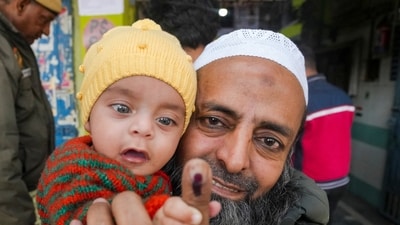 A voter carrying a child displays his inked finger after casting his vote at a polling station in Jafrabad during the Delhi Assembly election in New Delhi on Wednesday. (PTI) A voter carrying a child displays his inked finger after casting his vote at a polling station in Jafrabad during the Delhi Assembly election in New Delhi on Wednesday. (PTI)