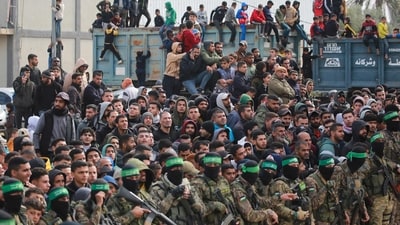 Hamas fighters stand in formation as Palestinians gather on a street to witness the handover of three Israeli hostages to a Red Cross team in Deir el-Balah, central Gaza, on February 8, 2025. (AFP) Hamas fighters stand in formation as Palestinians gather on a street to witness the handover of three Israeli hostages to a Red Cross team in Deir el-Balah, central Gaza, on February 8, 2025. (AFP)