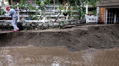 SIERRA MADRE, CALIFORNIA - FEBRUARY 14: A resident walks atop a mudslide along his home the morning after it tumbled down from the Eaton Fire burn zone during a powerful atmospheric river storm on February 14, 2025 in Sierra Madre, California. The storm impacted a widespread swathe of Southern California with some mandatory evacuations ordered over fears of rock slides and and debris flows in recent burn scar areas including hillside areas impacted by the Palisades and Eaton fires. Mario Tama/Getty Images/AFP (Photo by MARIO TAMA / GETTY IMAGES NORTH AMERICA / Getty Images via AFP) (Getty Images via AFP) SIERRA MADRE, CALIFORNIA - FEBRUARY 14: A resident walks atop a mudslide along his home the morning after it tumbled down from the Eaton Fire burn zone during a powerful atmospheric river storm on February 14, 2025 in Sierra Madre, California. The storm impacted a widespread swathe of Southern California with some mandatory evacuations ordered over fears of rock slides and and debris flows in recent burn scar areas including hillside areas impacted by the Palisades and Eaton fires. Mario Tama/Getty Images/AFP (Photo by MARIO TAMA / GETTY IMAGES NORTH AMERICA / Getty Images via AFP) (Getty Images via AFP)