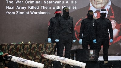 Masked Palestinian militants stand next to one of the coffins on stage, with an altered portrait of Israeli Premier Benjamin Netanyahu in the background, before handing over the bodies of four Israeli hostages to the Red Cross in Khan Yunis in the southern Gaza on February 20, 2025. (AFP) Masked Palestinian militants stand next to one of the coffins on stage, with an altered portrait of Israeli Premier Benjamin Netanyahu in the background, before handing over the bodies of four Israeli hostages to the Red Cross in Khan Yunis in the southern Gaza on February 20, 2025. (AFP)