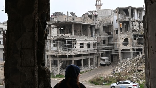 Displaced Syrian Umm Hamza Rifai, 56, looks at the destruction in her neighbourhood from her damaged apartment in Homs' Khaldiyeh district on February 10, 2025, following her return to the central Syrian city in the aftermath of the fall of Bashar al-Assad, after years of living away from their hometown in northern Syria. Since Assad's ouster in December 2024, Rifai and her family have been among thousands of people who have returned to neighbourhoods they fled in Homs during the civil war. (Photo by LOUAI BESHARA / AFP) (AFP)