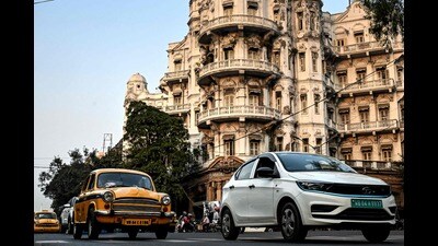 This photograph taken on January 27, 2025 shows Hindustan Ambassador yellow taxis (L) and a Tata Motors electric vehicle (EV) riding past the Esplanade Mansion, a heritage building in Kolkata. Kolkata cherishes its past, which is why the one-time Indian capital is mourning a vanishing emblem of its faded grandeur: a hulking and noisy fleet of stately yellow taxis. (Photo by Dibyangshu SARKAR / AFP) / To go with 'India-Culture-Automobile', FOCUS (AFP) This photograph taken on January 27, 2025 shows Hindustan Ambassador yellow taxis (L) and a Tata Motors electric vehicle (EV) riding past the Esplanade Mansion, a heritage building in Kolkata. Kolkata cherishes its past, which is why the one-time Indian capital is mourning a vanishing emblem of its faded grandeur: a hulking and noisy fleet of stately yellow taxis. (Photo by Dibyangshu SARKAR / AFP) / To go with 'India-Culture-Automobile', FOCUS (AFP)