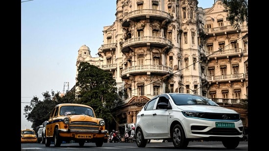 This photograph taken on January 27, 2025 shows Hindustan Ambassador yellow taxis (L) and a Tata Motors electric vehicle (EV) riding past the Esplanade Mansion, a heritage building in Kolkata. Kolkata cherishes its past, which is why the one-time Indian capital is mourning a vanishing emblem of its faded grandeur: a hulking and noisy fleet of stately yellow taxis. (Photo by Dibyangshu SARKAR / AFP) / To go with 'India-Culture-Automobile', FOCUS (AFP)