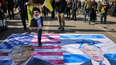An Iraqi mourner holds a portrait of the slain leader of the Lebanese Shiite Islamist Hezbollah movement Hassan Nasrallah as he walks over US (L) and Israeli (R) with pictures of US President Donald Trump and Israeli Prime Minister Benjamin Netanyahu during a symbolic funeral in the holy city of Kadhimiya in Baghdad on February 23, 2025. (AFP) An Iraqi mourner holds a portrait of the slain leader of the Lebanese Shiite Islamist Hezbollah movement Hassan Nasrallah as he walks over US (L) and Israeli (R) with pictures of US President Donald Trump and Israeli Prime Minister Benjamin Netanyahu during a symbolic funeral in the holy city of Kadhimiya in Baghdad on February 23, 2025. (AFP)