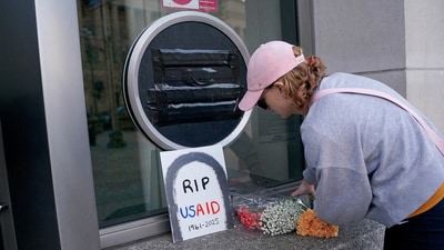 A person leaves flowers, next to a USAID sign which is covered over, at the agency's headquarters in Washington. (REUTERS)