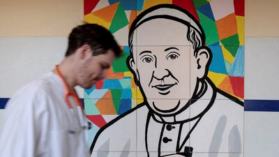 A man walks near a painting depicting Pope Francis at the Gemelli Hospital, where he is admitted for treatment, in Rome, Italy, March 3, 2025. (REUTERS)