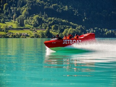 A jet boat glides across the waters of Lake Brienz, surrounded by lush green hills and alpine landscapes in Interlaken, Switzerland. A jet boat glides across the waters of Lake Brienz, surrounded by lush green hills and alpine landscapes in Interlaken, Switzerland.
