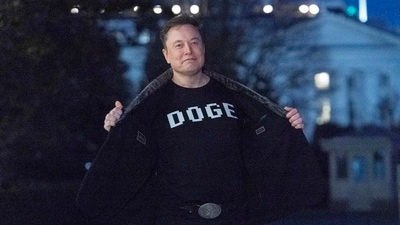 Elon Musk flashes his t-shirt that reads "DOGE" to the media as he walks on South Lawn of the White House, in Washington. (AP) Elon Musk flashes his t-shirt that reads "DOGE" to the media as he walks on South Lawn of the White House, in Washington. (AP)