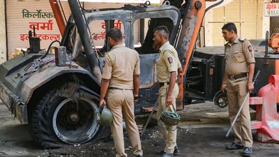 Nagpur: Police personnel near charred remains of a vehicle, a day after violence broke out following an agitation by a right-wing group demanding removal of Aurangzeb's tomb, in Nagpur. (PTI) Nagpur: Police personnel near charred remains of a vehicle, a day after violence broke out following an agitation by a right-wing group demanding removal of Aurangzeb's tomb, in Nagpur. (PTI)