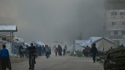 Surrounded by smoke from a nearby Israeli army strike, Palestinians walk past tents in central Gaza City on Saturday, March 22, 2025. (AP) Surrounded by smoke from a nearby Israeli army strike, Palestinians walk past tents in central Gaza City on Saturday, March 22, 2025. (AP)