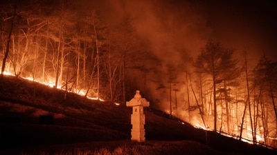 A wildfire is seen next to a stone lantern of family tomb in Andong on March 26, 2025.. (AFP) A wildfire is seen next to a stone lantern of family tomb in Andong on March 26, 2025.. (AFP)