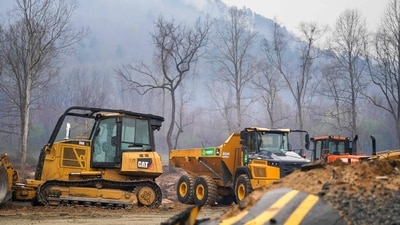 SALUDA, NORTH CAROLINA - MARCH 24: Smoke rises from a mountain ridge near storm debris and heavy machinery at the Black Cove wildfire on March 24, 2025 in Polk County near Saluda, North Carolina. Recovery efforts continue along the Green River in Western North Carolina nearly six months after Hurricane Helene. (Photo by Sean Rayford / GETTY IMAGES NORTH AMERICA / Getty Images via AFP) (Getty Images via AFP) SALUDA, NORTH CAROLINA - MARCH 24: Smoke rises from a mountain ridge near storm debris and heavy machinery at the Black Cove wildfire on March 24, 2025 in Polk County near Saluda, North Carolina. Recovery efforts continue along the Green River in Western North Carolina nearly six months after Hurricane Helene. (Photo by Sean Rayford / GETTY IMAGES NORTH AMERICA / Getty Images via AFP) (Getty Images via AFP)