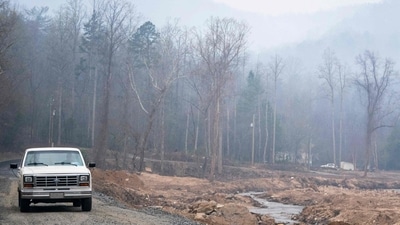 SALUDA, NORTH CAROLINA - MARCH 24: A motorist navigate a flood damaged road as smoke hangs in the air near the Black Cove wildfire on March 24, 2025 in Polk County near Saluda, North Carolina. Recovery efforts continue along the Green River in Western North Carolina nearly six months after Hurricane Helene. Three large wildfires have burned more than 3,000 acres as evacuation orders were issued for parts of Polk County (Photo by Sean Rayford / GETTY IMAGES NORTH AMERICA / Getty Images via AFP) (Getty Images via AFP) SALUDA, NORTH CAROLINA - MARCH 24: A motorist navigate a flood damaged road as smoke hangs in the air near the Black Cove wildfire on March 24, 2025 in Polk County near Saluda, North Carolina. Recovery efforts continue along the Green River in Western North Carolina nearly six months after Hurricane Helene. Three large wildfires have burned more than 3,000 acres as evacuation orders were issued for parts of Polk County (Photo by Sean Rayford / GETTY IMAGES NORTH AMERICA / Getty Images via AFP) (Getty Images via AFP)