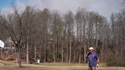 ROCKY BOTTOM, SOUTH CAROLINA - MARCH 26: Smoke rises from the Table Rock Complex fire as a man plays golf on March 26, 2025 in Rocky Bottom, South Carolina. Drought-like conditions and high winds are fueling multiple wildfires that have triggered evacuations across northern South Carolina. (Photo by Sean Rayford / GETTY IMAGES NORTH AMERICA / Getty Images via AFP) (Getty Images via AFP) ROCKY BOTTOM, SOUTH CAROLINA - MARCH 26: Smoke rises from the Table Rock Complex fire as a man plays golf on March 26, 2025 in Rocky Bottom, South Carolina. Drought-like conditions and high winds are fueling multiple wildfires that have triggered evacuations across northern South Carolina. (Photo by Sean Rayford / GETTY IMAGES NORTH AMERICA / Getty Images via AFP) (Getty Images via AFP)