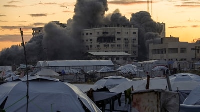 Behind a tent camp for displaced Palestinians, smoke rises from a building after it was targeted by an Israeli army strike in Gaza City. (AP file) Behind a tent camp for displaced Palestinians, smoke rises from a building after it was targeted by an Israeli army strike in Gaza City. (AP file)
