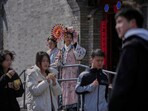 People walk by workers dressed in Qing Dynasty costumes, one of them holding a fan to attract customers outside a merchandise shop, in Beijing.