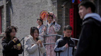 People walk by workers dressed in Qing Dynasty costumes, one of them holding a fan to attract customers outside a merchandise shop, in Beijing. (AP) People walk by workers dressed in Qing Dynasty costumes, one of them holding a fan to attract customers outside a merchandise shop, in Beijing. (AP)