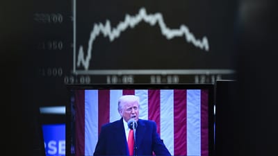 Behind a television monitor showing U.S. President Donald Trump, the display board with the Dax curve shows falling share prices, in Frankfurt (AP) Behind a television monitor showing U.S. President Donald Trump, the display board with the Dax curve shows falling share prices, in Frankfurt (AP)