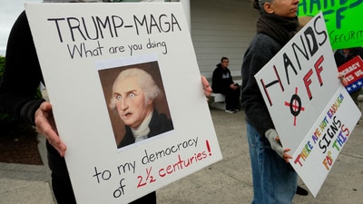 Holding a placard with an image of former President George Washington, a demonstrator attends a "Hands Off" protest (REUTERS)