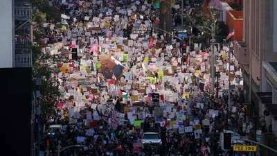 Protesters hold signs and flags and a large balloon with an image of US President Donald Trump during the nationwide "Hands Off!" protest against Trump and his advisor, Tesla CEO Elon Musk, in downtown Los Angeles on April 5, 2025.  (AFP)