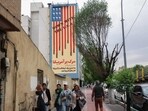 People walk along Tehran's Karim Khan Zand Avenue past a building with a landmark anti-US mural with the slogan "Down with the USA" and skulls replacing the stars on the US flag, on April 12, 2025. Iran's top diplomat arrived in Oman on April 12 and began laying the groundwork for high-stakes nuclear talks with the United States that are unfolding under the threat of military action.