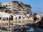 People walk past a puddle of water by tent shelters erected near the rubble of a collapsed building in the Nasr neighbourhood in western Gaza City on April 15, 2025.