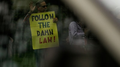 A demonstrator holding a placard is visible through the window of a passing vehicle at a protest against US President Donald Trump and Vice President JD Vance, at the US Naval Observatory, the Vice President's official residence,&nbsp; (REUTERS)