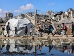 People walk past a puddle of water by a tent shelter erected near the rubble of a collapsed building in the Nasr neighbourhood in western Gaza City on April 15, 2025. People walk past a puddle of water by a tent shelter erected near the rubble of a collapsed building in the Nasr neighbourhood in western Gaza City on April 15, 2025.