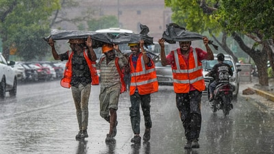 Workers huddle together under a plastic sheet during rainfall, in New Delhi. (PTI) Workers huddle together under a plastic sheet during rainfall, in New Delhi. (PTI)