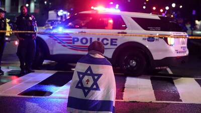 A man, with an Israeli flag with a cross in the center, kneels next to emergency personnel working at the site where two Israeli embassy staff were shot dead near the Capital Jewish Museum in Washington. (REUTERS)