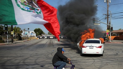 The deployment followed two days of clashes over immigration raids, during which federal agents used tear gas and flash-bang grenades. In pic: A Mexican flag waves as a car burns in flames following multiple detentions by Immigration and Customs Enforcement (ICE), in the Los Angeles County, (REUTERS)