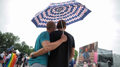 Two men shared a warm side hug beneath a single umbrella as they attended the WorldPride International Rally and March on Washington for Freedom at the Lincoln Memorial on June 8, 2025. (Photo by Kayla Bartkowski / GETTY IMAGES NORTH AMERICA / Getty Images via AFP) (Getty Images via AFP)