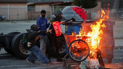 Protesters stand next to a burning shopping cart during a standoff between police and protesters following multiple detentions by Immigration and Customs Enforcement (ICE), in the Los Angeles County city of Compton. (REUTERS)