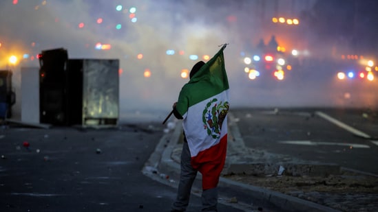 Governor Newsom urged peaceful protest, warning, “Federal authorities want a spectacle. Don’t give them one.” In pic: A protester holds a Mexican flag during a standoff between police and protesters following multiple detentions by Immigration and Customs Enforcement (ICE), in the Los Angeles County city of Compton.(REUTERS)