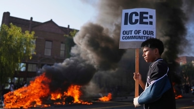 A protester holds a sign as a Waymo taxi burns near the metropolitan detention center of downtown Los Angeles, Sunday, June 8, 2025, following last night's immigration raid protest. (AP Photo/Eric Thayer) (AP) A protester holds a sign as a Waymo taxi burns near the metropolitan detention center of downtown Los Angeles, Sunday, June 8, 2025, following last night's immigration raid protest. (AP Photo/Eric Thayer) (AP)
