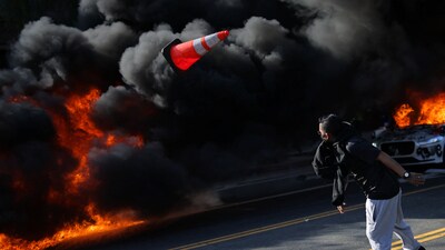 A protester throws a traffic cone as fires burn during demonstrations against federal immigration raids in downtown Los Angeles. (REUTERS)