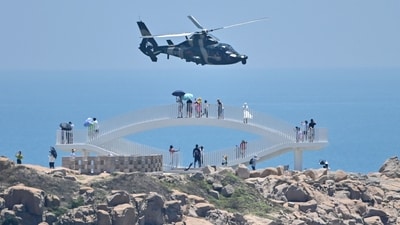 Tourists look on as a Chinese military helicopter flies past Pingtan island, one of mainland China's closest point from Taiwan, in Fujian province on August 4, 2022, ahead of massive military drills off Taiwan following US House Speaker Nancy Pelosi's visit to the self-ruled island. China is due on August 4 to kick off its largest-ever military exercises encircling Taiwan, in a show of force straddling vital international shipping lanes following a visit to the self-ruled island by US House Speaker Nancy Pelosi. (Photo by Hector RETAMAL / AFP) Tourists look on as a Chinese military helicopter flies past Pingtan island, one of mainland China's closest point from Taiwan, in Fujian province on August 4, 2022, ahead of massive military drills off Taiwan following US House Speaker Nancy Pelosi's visit to the self-ruled island. China is due on August 4 to kick off its largest-ever military exercises encircling Taiwan, in a show of force straddling vital international shipping lanes following a visit to the self-ruled island by US House Speaker Nancy Pelosi. (Photo by Hector RETAMAL / AFP)