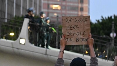 A persons holds a sign reading "We Were Here Before Your Border" as Los Angeles Police Department officers clear an overpass bridge on June 10, 2025. (AFP) A persons holds a sign reading "We Were Here Before Your Border" as Los Angeles Police Department officers clear an overpass bridge on June 10, 2025. (AFP)