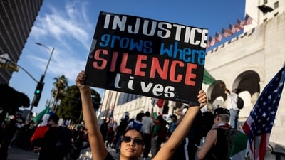 A demonstrator holds a sign reading "Injustice grows where silence lives" in front of City Hall as protests continue in response to federal immigration operations in Los Angeles on June 13, 2025. (AFP) A demonstrator holds a sign reading "Injustice grows where silence lives" in front of City Hall as protests continue in response to federal immigration operations in Los Angeles on June 13, 2025. (AFP)