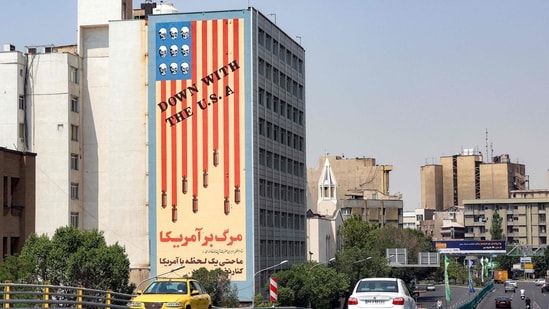 Vehicles move along the Karim Khan Zand Bridge past the 'Down with the USA' mural painted on the side of the National Organisation of Educational Testing building in central Tehran on June 13, 2025. Israel unleashed a wave of strikes on Iran on June 13, hitting about 100 targets including nuclear facilities and military command centres, and killing senior figures, among them the armed forces chief and top nuclear scientists.(AFP)