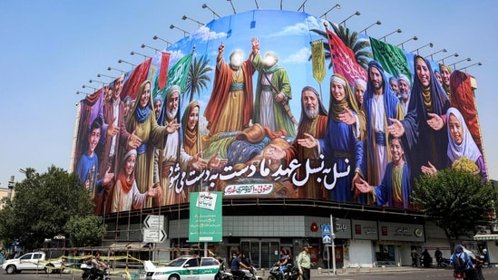A traffic policeman walks as motorists drive past a mural commemorating the Shiite Muslim holiday of Eid al-Ghadir, when according to Shiite belief the Islamic prophet Mohamed designated his nephew and companion Ali ibn Abi Talib as his successor, in Enghelab (Revolution) Square in central Tehran on June 13, 2025. Israel unleashed a wave of strikes on Iran on June 13, hitting about 100 targets including nuclear facilities and military command centres, and killing senior figures, among them the armed forces chief and top nuclear scientists.(AFP)