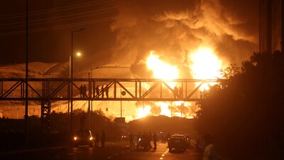 People watch from a bridge as flames from an Israeli attack rise from Sharan Oil depot, following Israeli strikes on Iran, in Tehran, Iran, June 15, 2025. (REUTERS)