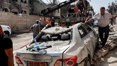 Men walk near a damaged vehicle at an impact site following missile attack from Iran, in northern Israel, in Tamra, Israel, June 15, 2025. (REUTERS)